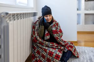 woman-on-phone-with-blanket-and-hat-sits-by-radiator